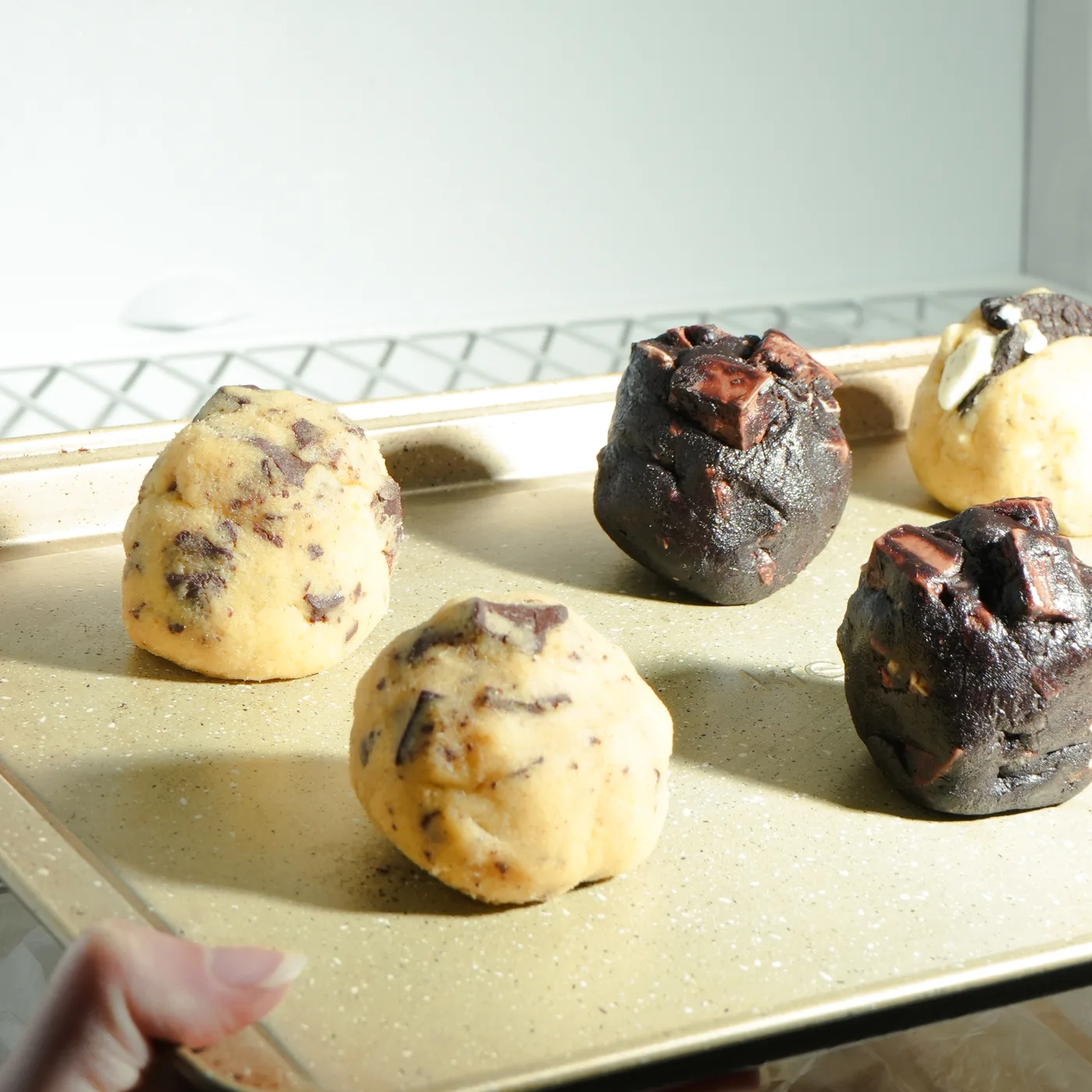 Bolitas de masa de cookies congeladas de distintos sabores sobre una placa, listas para hornear
